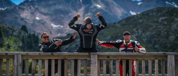 Drei Motorradfahrer posieren vor Berglandschaft auf einer Holzplattform