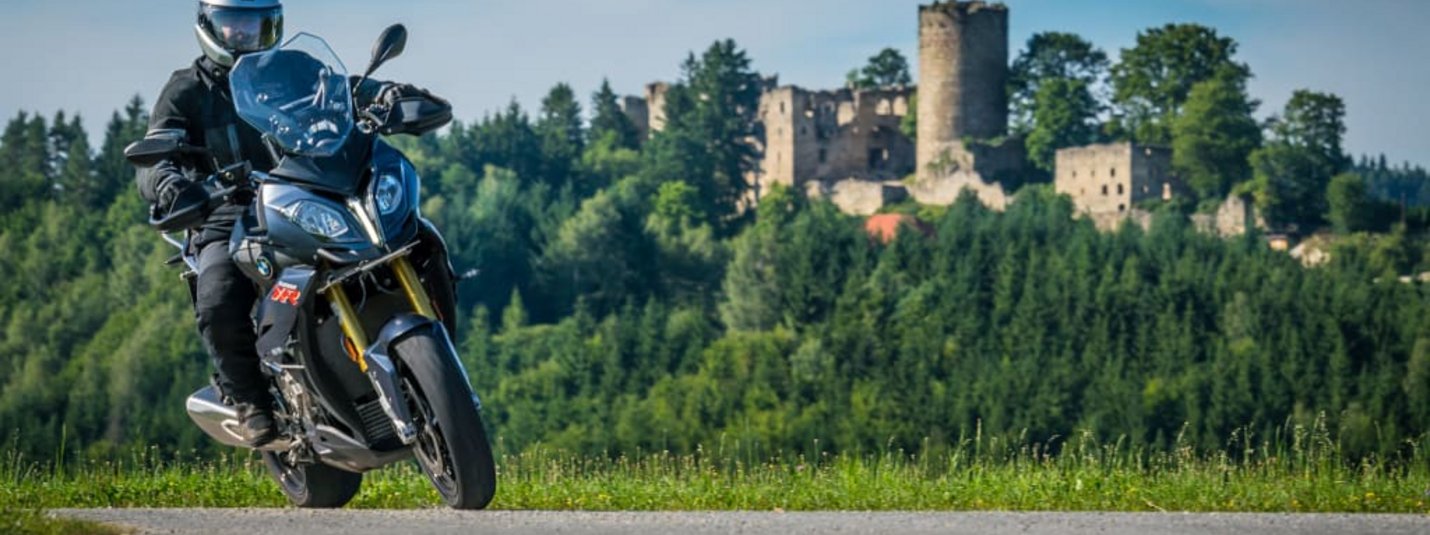 Kurvenreich Motorradwoche Motorradfahrer fährt vor einer Burg und bewaldeter Landschaft