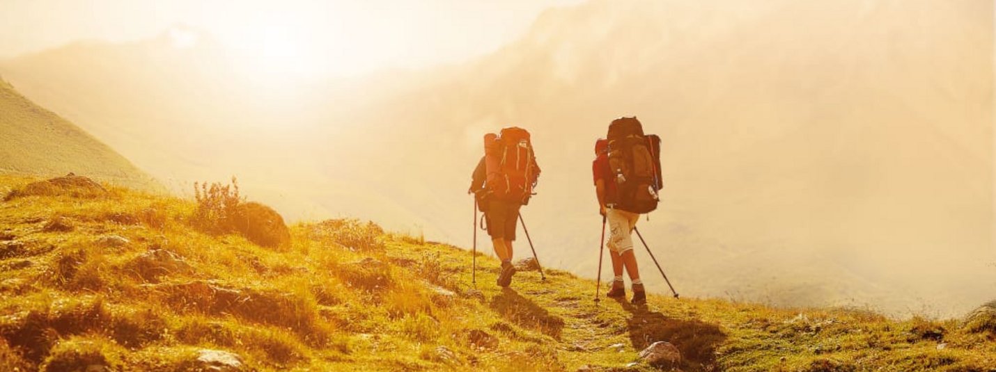 Aktivurlaub für Erlebnissammler - 7 Nächte Zwei Wanderer mit Rucksäcken wandern auf einem sonnigen Bergweg