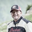 Roland Schöpf © studio22.at - Marcel Hagen Lächelnder Mann mit Motorrad in Berglandschaft