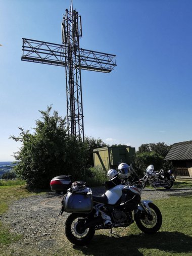 Motorräder vor einem großen metallischen Kreuz auf einem Hügel