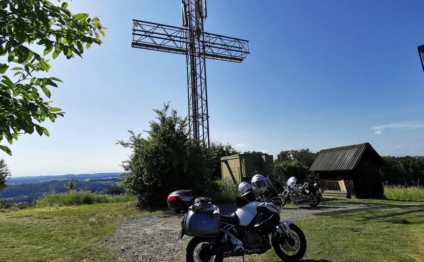 Motorräder vor einem großen metallischen Kreuz auf einem Hügel