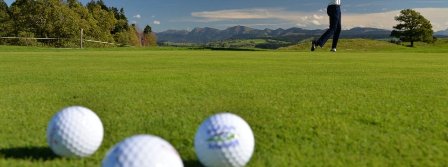 Golfschnupperkurs Golfspieler beim Abschlag auf grünem Golfplatz mit Bergen im Hintergrund