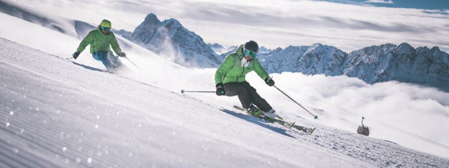 Wellness Power Package 5=4 Zwei Skifahrer fahren einen schneebedeckten Hang in den Bergen hinunter