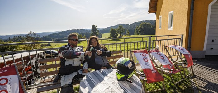 Motorradfahrer genießen sonnige Pause mit Getränken auf Terrasse mit Bergblick