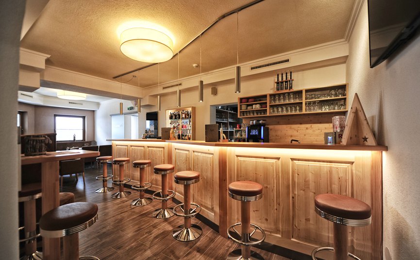 Bar mit Holztheke und Barhockern in warm beleuchtetem Raum