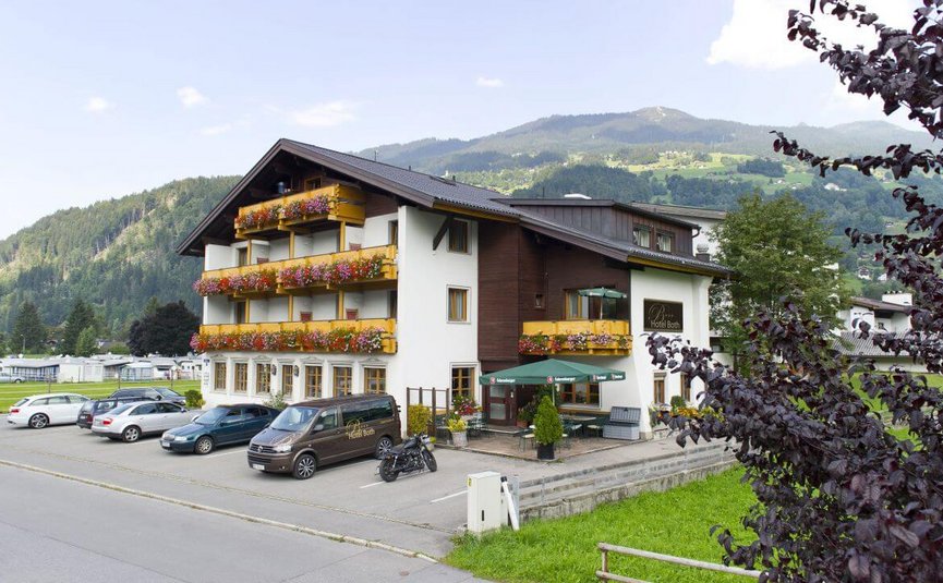 Hotelgebäude mit Balkonblumen und Bergen im Hintergrund