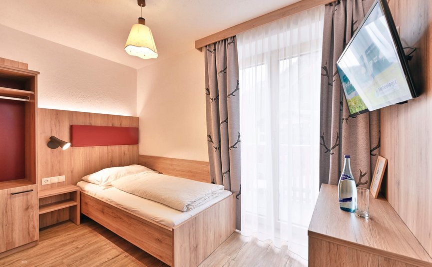 Kleines modernes Einzelzimmer mit Bett, TV und Fenster mit Vorhängen