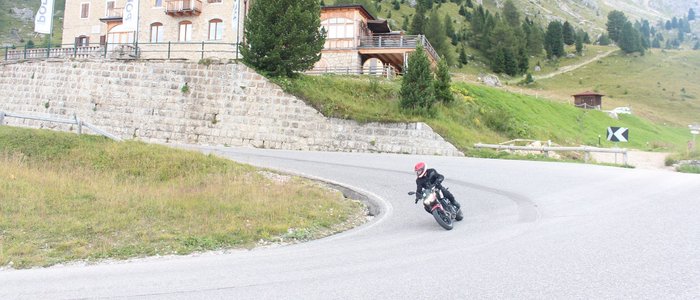 Motorradfahrer fährt auf kurviger Bergstraße am Hotel Pordoi
