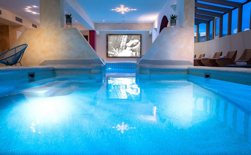 Vötter's Hotel **** © Nikolaus Faistauer Innenpool mit blauem Wasser und Liegestühlen in einer Spa-Lounge