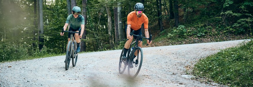 Zwei Radfahrer fahren auf einem Waldweg auf schottriger Strecke