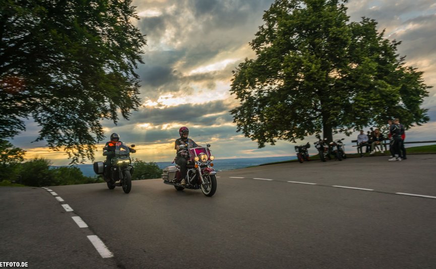 Motorradurlaub in Bayern © Moppetfoto.de Zwei Motorradfahrer fahren bei Sonnenuntergang an einer Kurve vorbei.