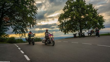 Bayern © Moppetfoto.de Zwei Motorradfahrer fahren bei Sonnenuntergang an einer Kurve vorbei.
