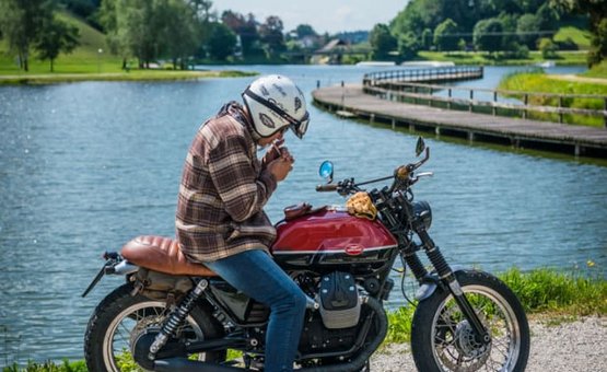 Wald4teler Kurvengaudi Mann mit Helm zündet Zigarette an, sitzt auf rotem Motorrad am See