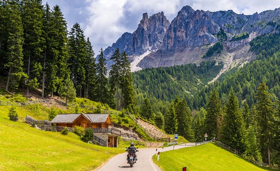 Motorradurlaub in der Region 3 Zinnen – Kronplatz – Eisacktal © Alexander Seger Motorradfahrer auf kurviger Straße in den Bergen mit Holzhütte und Nadelbäumen