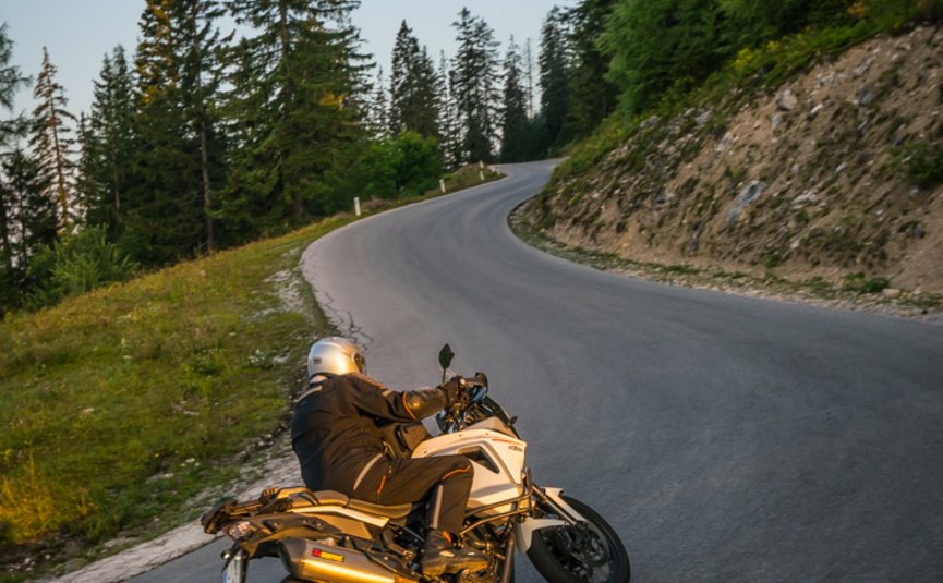 Motorradfahrer fährt eine Kurve auf bergiger Straße bei Sonnenuntergang