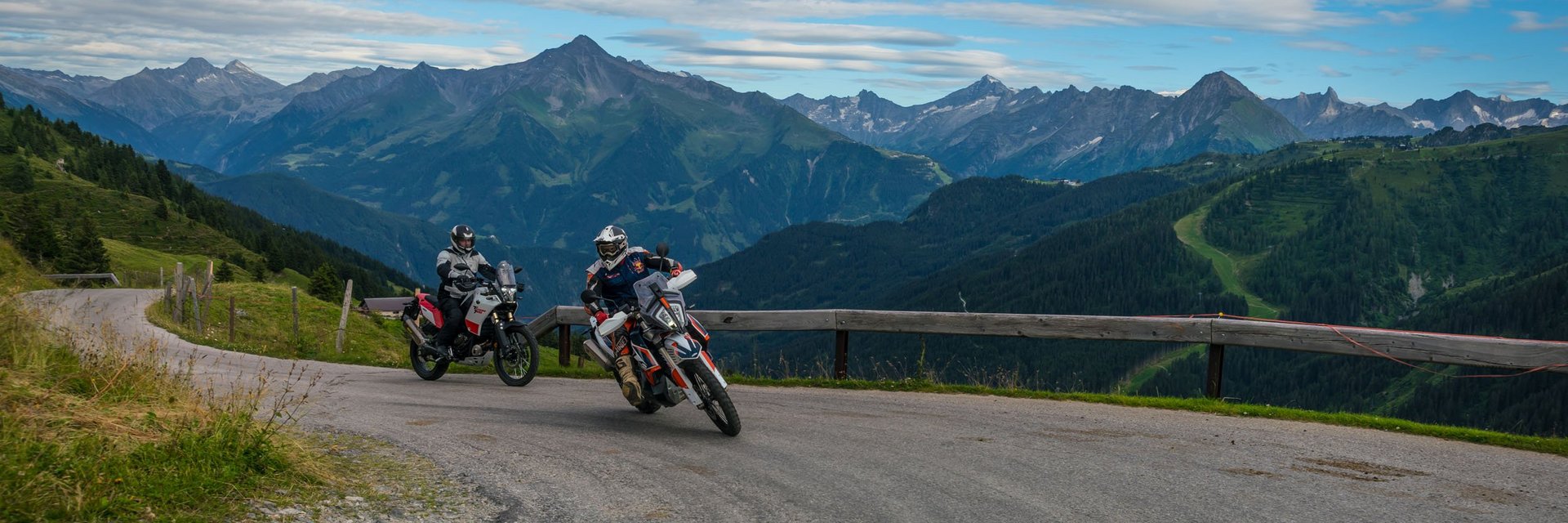 Zwei Motorradfahrer fahren auf Bergstraße mit Alpen im Hintergrund