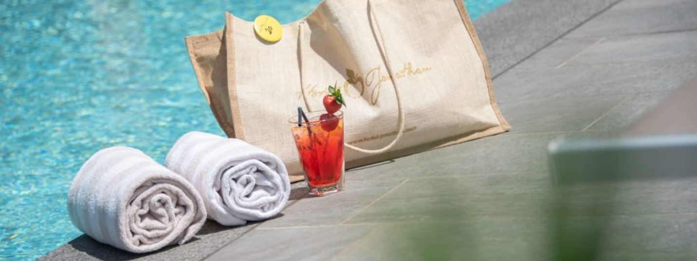 Zwei weiße Handtücher, eine Tasche und ein Cocktail am Poolrand