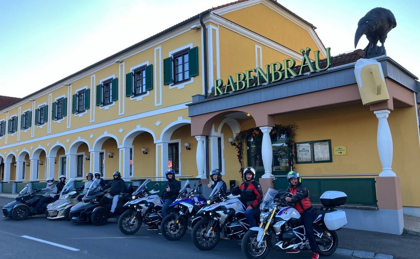 Motorradfahrer vor gelbem Gebäude mit Schild RABENBRÄU
