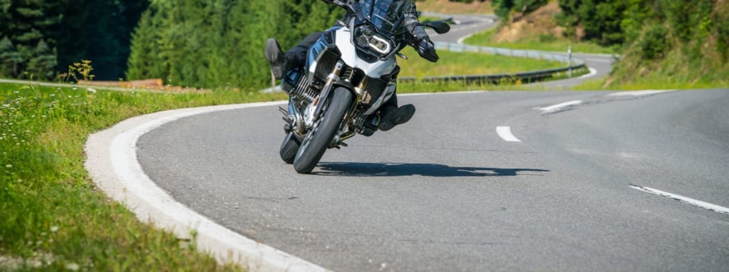 KURVENQUICKY Motorradfahrer fährt kurvige Straße in bergiger Landschaft