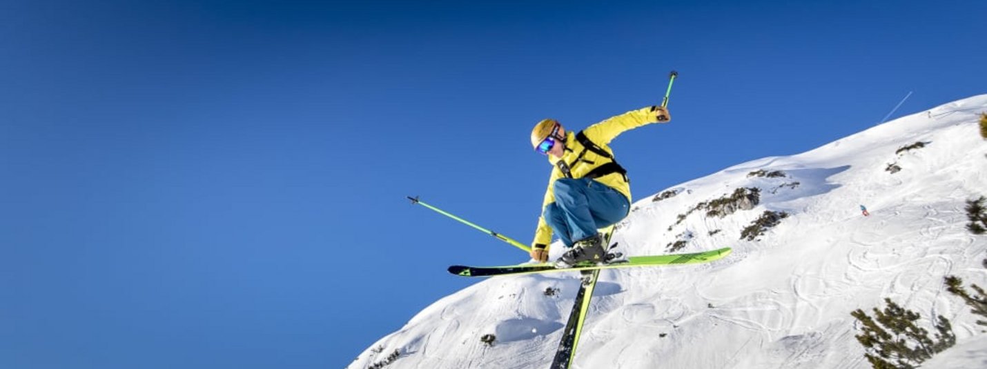 Mid-Week-Skitage 4 Skifahrer in gelber Jacke macht Sprung an verschneitem Berg bei klarem Himmel