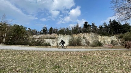 Gravelwoche Bucklige Welt © Landgasthof Krumbacherhof Radfahrer fährt auf Schotterweg vor bewaldetem Hang unter blauem Himmel