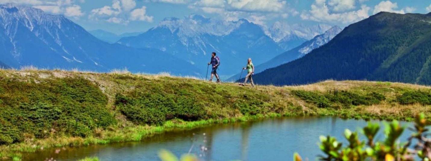Aktivurlaub für Erlebnissammler - 5 Nächte Zwei Wanderer am Bergsee mit Alpen und blauem Himmel im Hintergrund