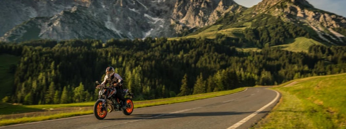 6 Tage "Maut inklusive" Motorradfahrer auf Bergstraße vor Felsen und Wald