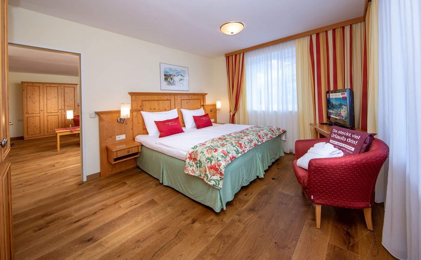 Vötter's Hotel **** © Nikolaus Faistauer Gemütliches Hotelzimmer mit Doppelbett, Holzmöbeln und rotem Sessel