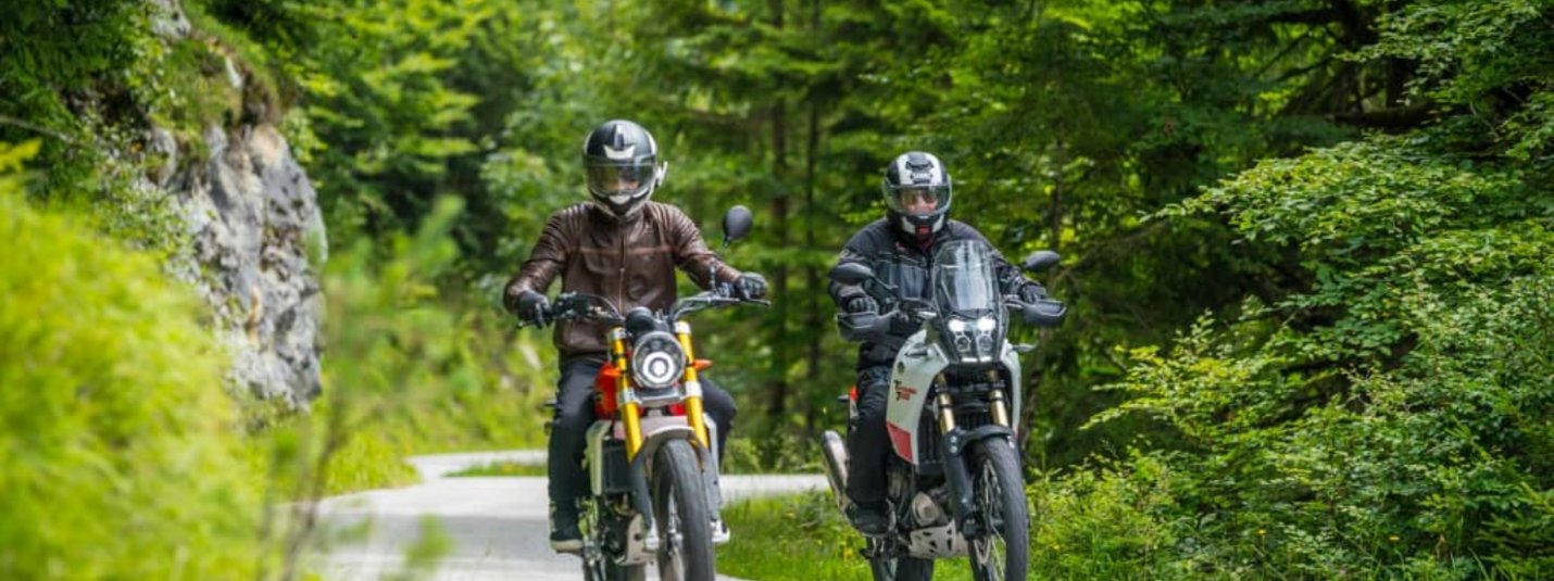 Kurvenwochenende Zwei Motorradfahrer fahren auf einer Straße durch einen grünen Wald