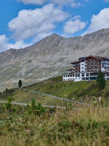 Alpenhotel am Hang mit Bergpanorama unter blauem Himmel