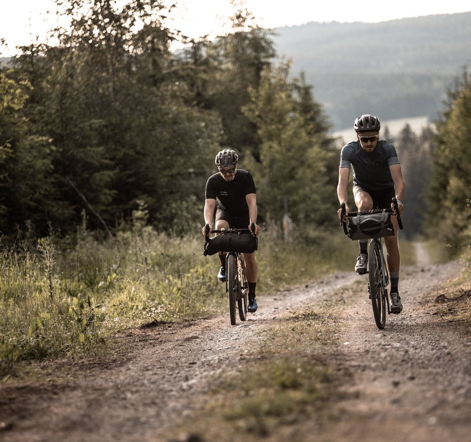 2. Women's Gravelcamp am Sportpark Rabenberg © Martin Matula Zwei Radfahrer fahren auf einem Waldweg bei bewölktem Himmel