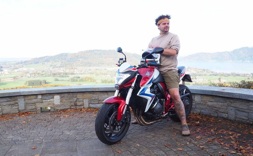 Gast-Hof-Laden Schneeweiss *** © Gast-Hof-Laden Schneeweiss Mann lehnt an rotem Motorrad mit Bergpanorama im Hintergrund