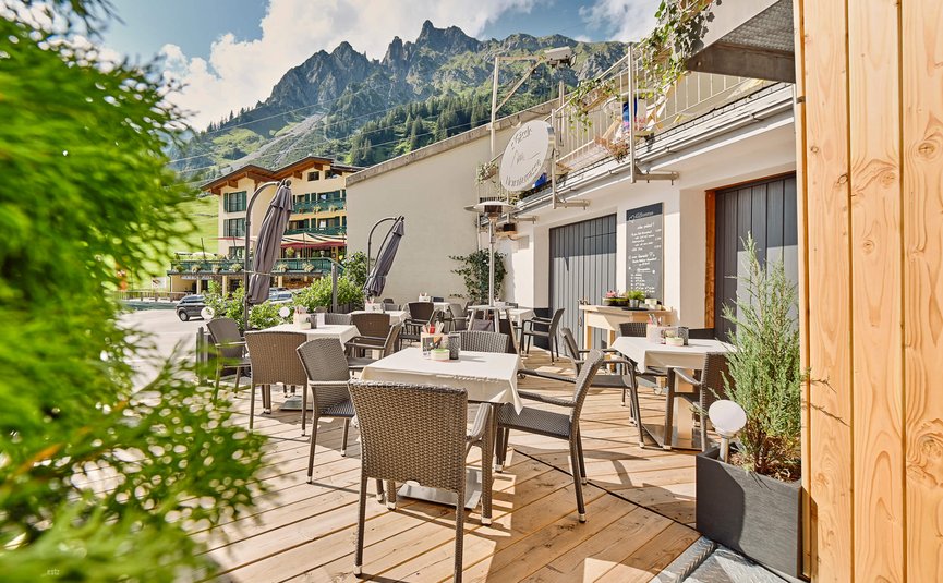 Außenbereich eines Cafés mit Tischen, Stühlen und Bergblick bei sonnigem Wetter