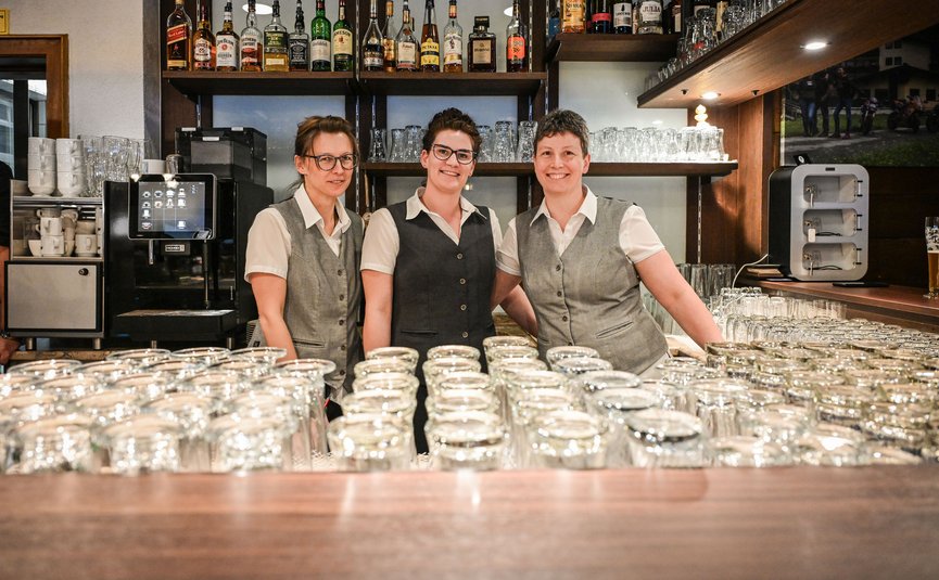 Drei Kellnerinnen stehen hinter einer Bar mit vielen Gläsern