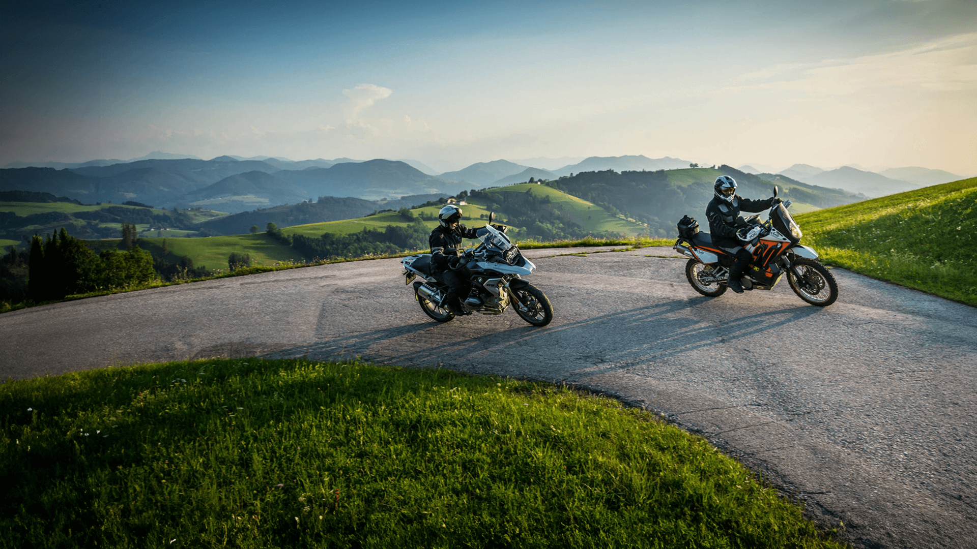 Zwei Motorradfahrer auf kurviger Bergstraße bei sonnigem Wetter