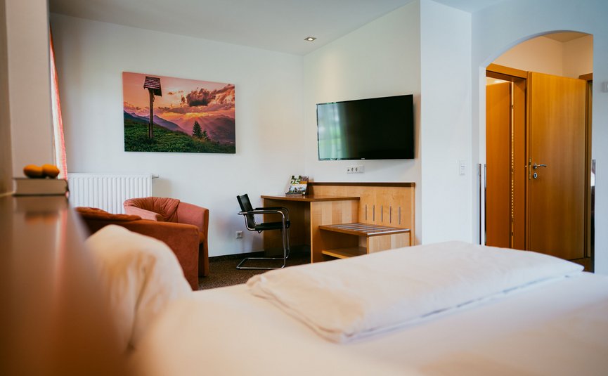 Blick auf ein helles Hotelzimmer mit Bett, Fernseher und Sitzbereich
