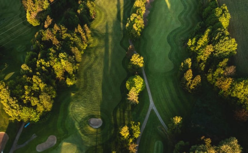 Golfwoche Luftaufnahme eines Golfplatzes mit Bäumen und langen Schatten bei Sonnenuntergang