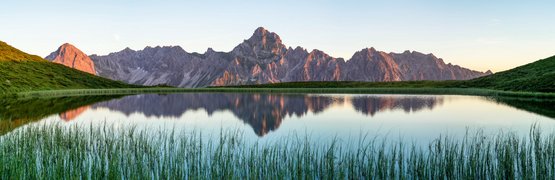 Bergspitzen spiegeln sich in einem ruhigen See umgeben von grünen Hügeln