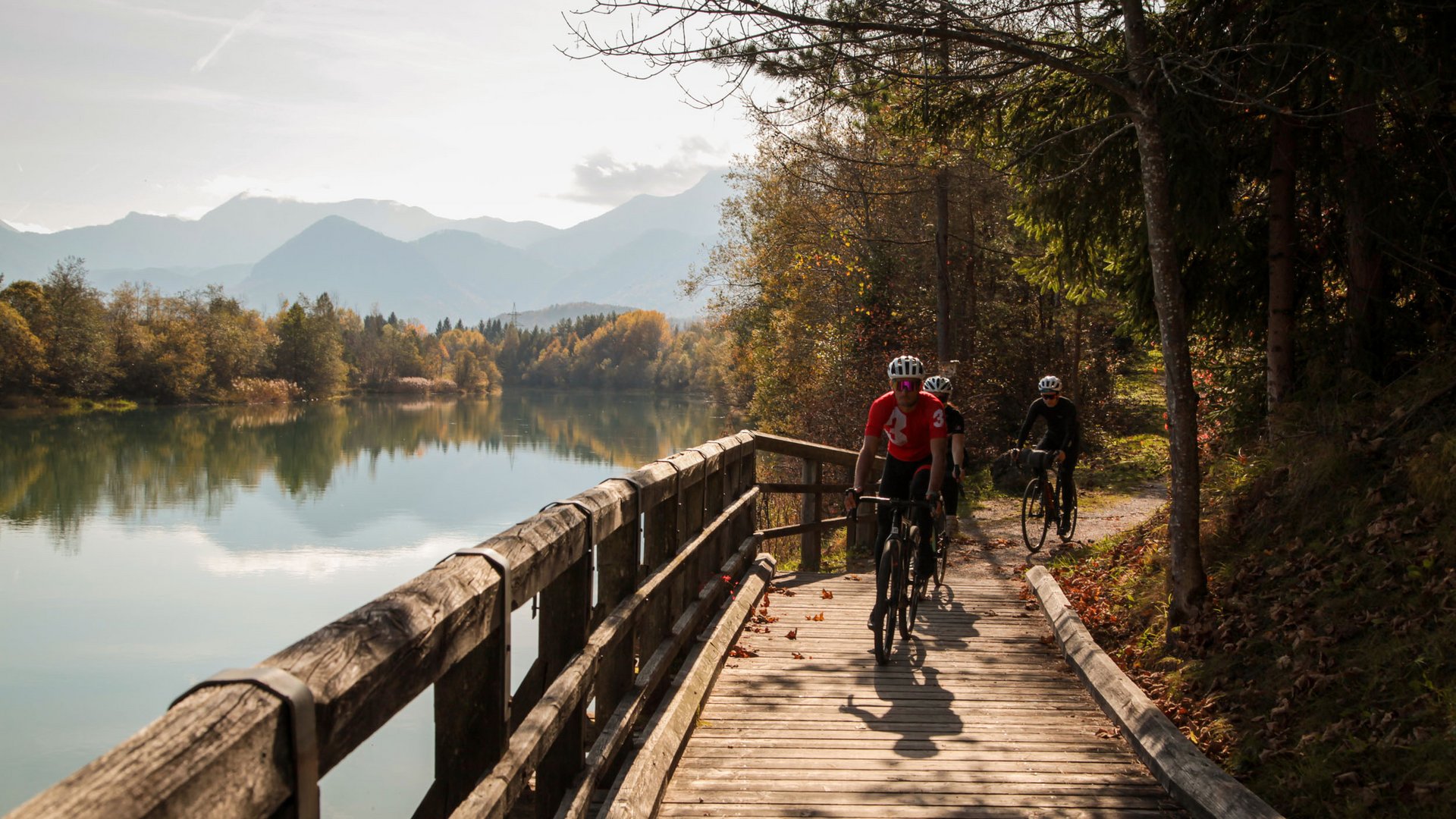 Gravel-Wundertüte Wörthersee © Wörthersee Tourismus GmbH - Christian Riedel Drei Radfahrer fahren auf Holzsteg neben See in herbstlicher Landschaft