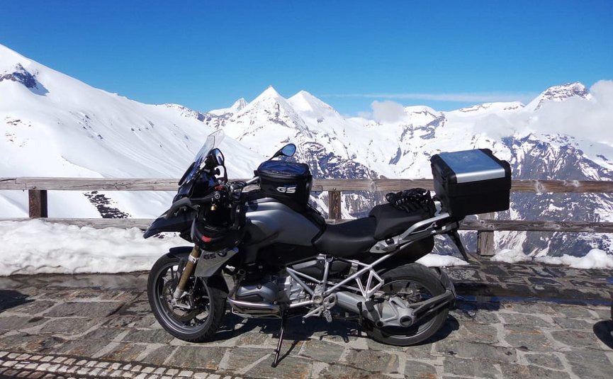 Kurvenkönig Special ab € 208,- pro Person Motorrad auf gepflastertem Weg mit schneebedeckten Bergen im Hintergrund