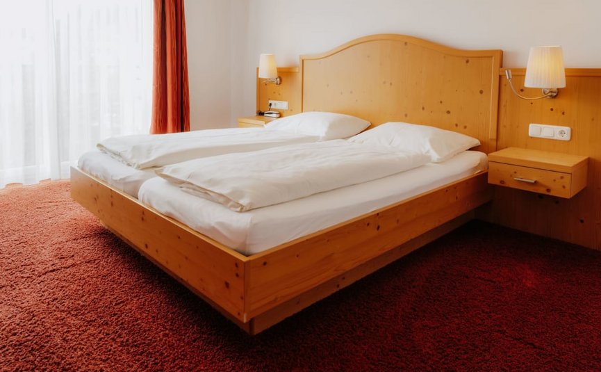 Goldener Herbst auf der Mühl4tler Alm Hotelzimmer mit Doppelbett aus hellem Holz und roten Teppichboden