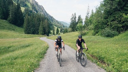 Grenzenlos graveln in Vorarlberg © Ian Ehm - Vorarlberg Tourismus Zwei Radfahrer fahren auf einem Schotterweg durch eine grüne Berglandschaft