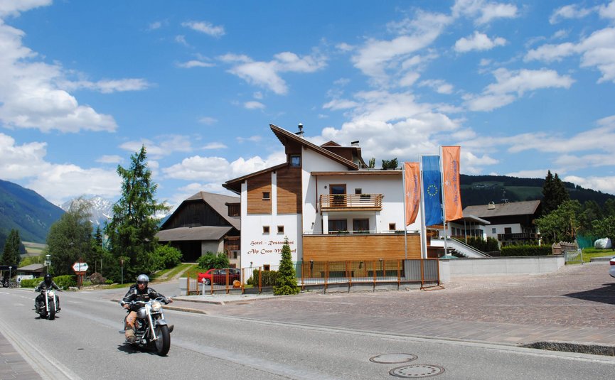 MOAR'S Hotel ***S © Moar's Hotel in Olang Motorradfahrer fahren an einem Hotel in den Bergen bei sonnigem Wetter vorbei