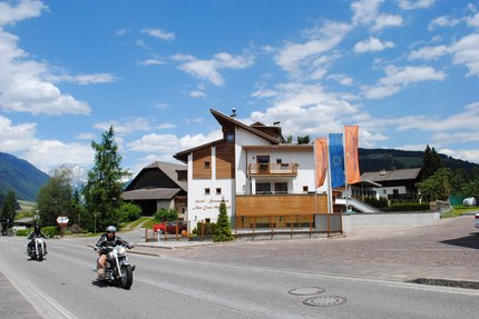 MOAR'S Hotel © Moar's Hotel in Olang Motorradfahrer fahren an einem Hotel in den Bergen bei sonnigem Wetter vorbei
