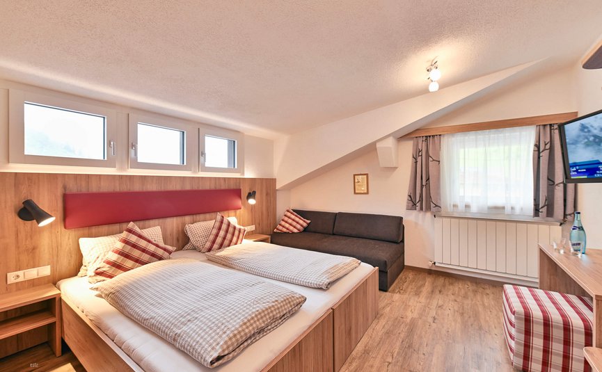Gemütliches Hotelzimmer mit Doppelbett und Couch unter Dachschräge