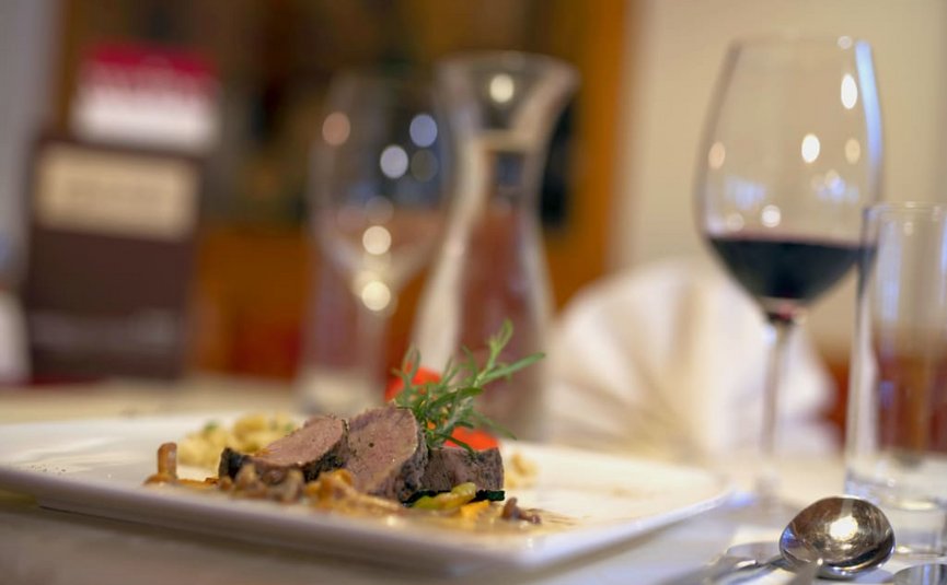 Babymoon im Hotel Rockenschaub Gedeckter Tisch mit Fleisch, Wein und Besteck in einem Restaurant.