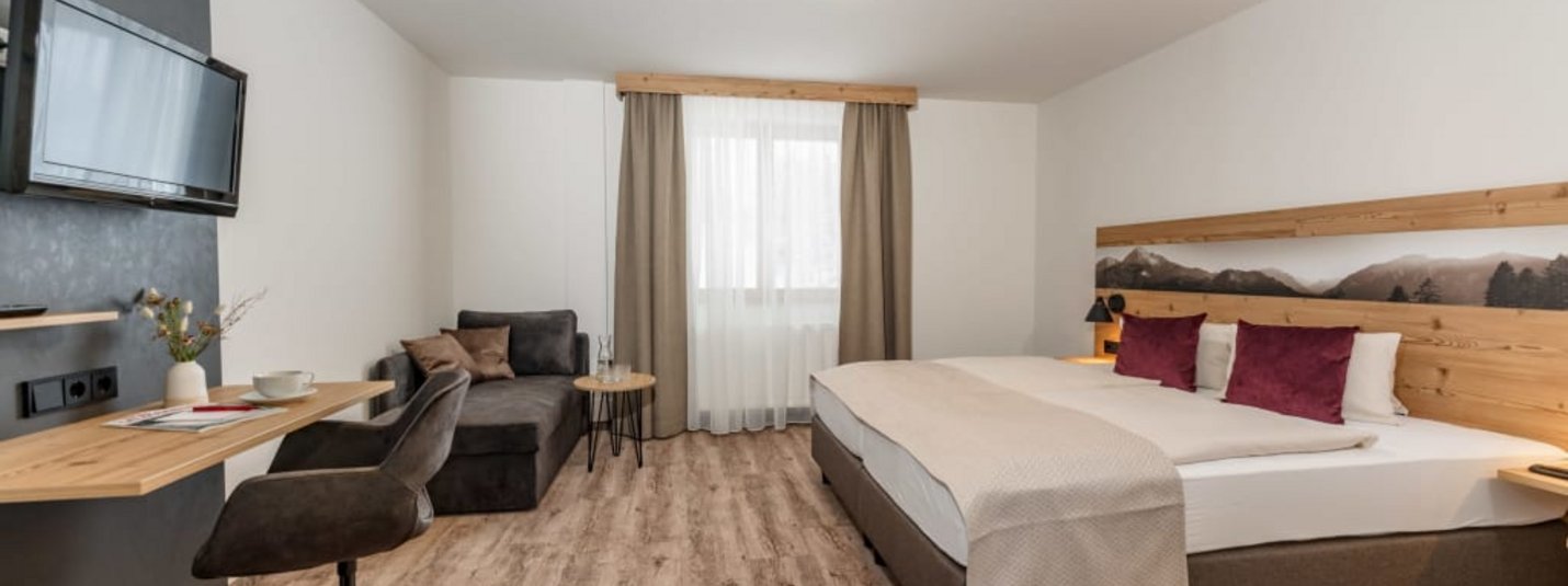 Modernes Hotelzimmer mit Doppelbett, Fernseher, Tisch und gemütlicher Sitzecke