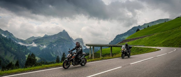 Zwei Motorräder auf bergiger Straße unter bewölktem Himmel