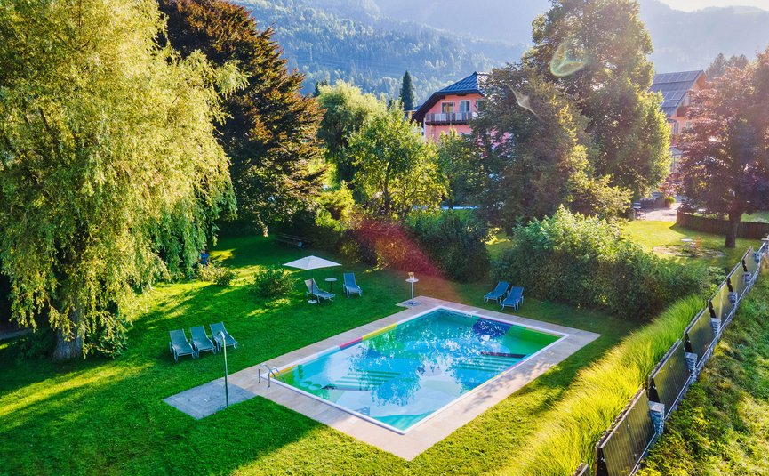 Schwimmbad im Garten mit Sonnenliegen und grünem Rasen umgeben von Bäumen